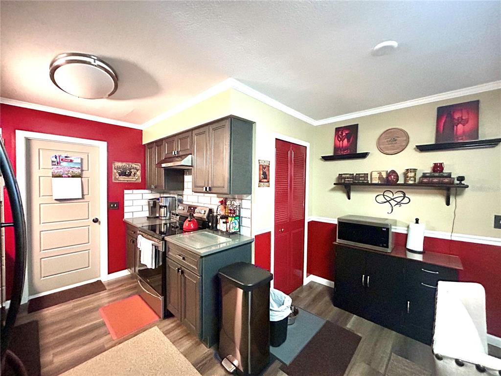 A kitchen features dark gray cabinets, red accent walls, stainless steel appliances, and open shelving — 2210 MURDOCK BOULEVARD, ORLANDO, FL
