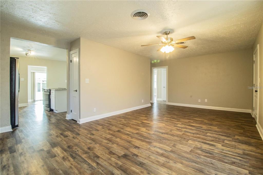 A living room with wood-look flooring, a ceiling fan, and doorways leading to other rooms — 1851 E ELM ROAD, LAKELAND, FL