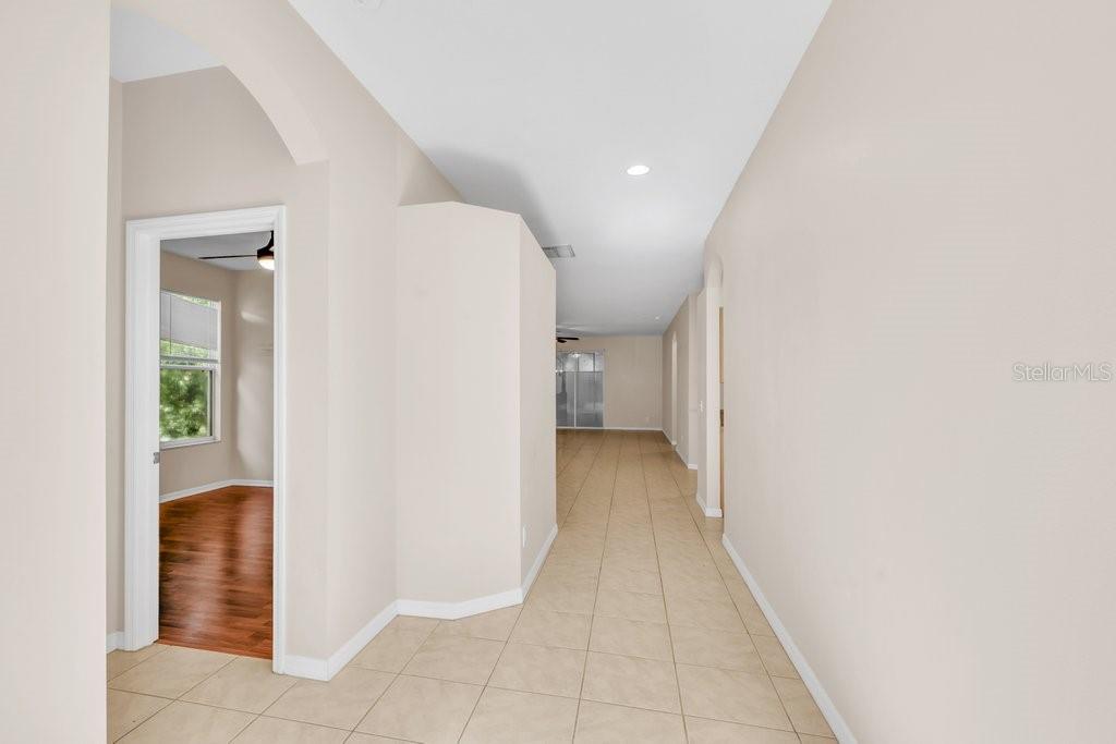 A hallway with light-colored tile flooring leads toward a room with a glass sliding door — 6105 GANNETSIDE PLACE, LITHIA, FL