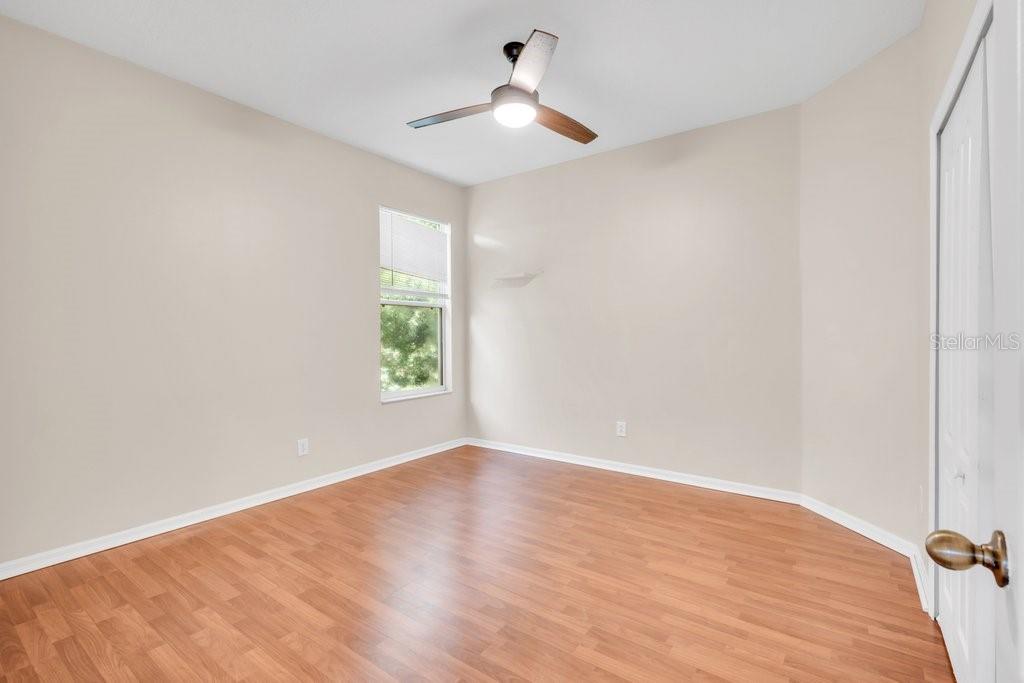An empty bedroom features light-colored walls, wood-look flooring, a ceiling fan, and a window — 6105 GANNETSIDE PLACE, LITHIA, FL