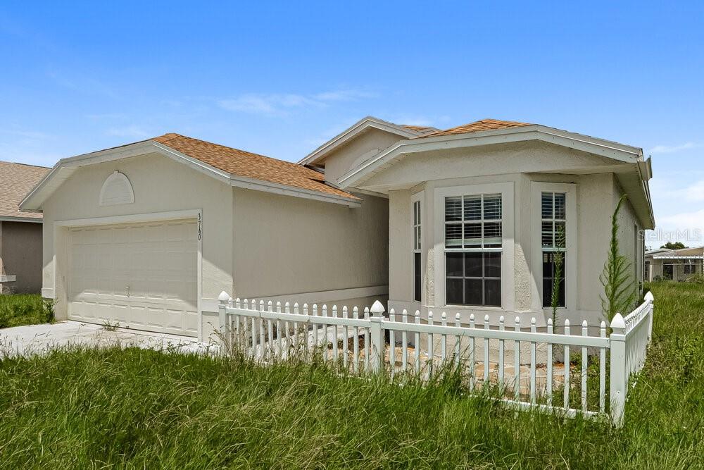 A single-story house with a white stucco exterior, a two-car garage, and a white fence — 3740 IMPERIAL DRIVE, WINTER HAVEN, FL