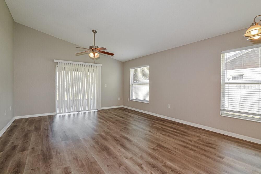 An empty living room with wood-look flooring, a vaulted ceiling, and a sliding glass door — 3740 IMPERIAL DRIVE, WINTER HAVEN, FL