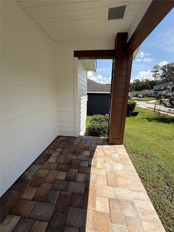 A covered porch features light-colored horizontal siding, a dark wooden support post, and paver flooring — 11348 NW 31ST LANE, GAINESVILLE, FL