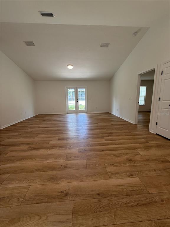An empty room features wood-look flooring, vaulted ceilings, and glass double doors leading outside — 11348 NW 31ST LANE, GAINESVILLE, FL