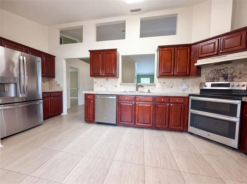 A kitchen features dark wood cabinets, stainless steel appliances, and light-colored tile flooring — 944 NW 87TH DRIVE, GAINESVILLE, FL