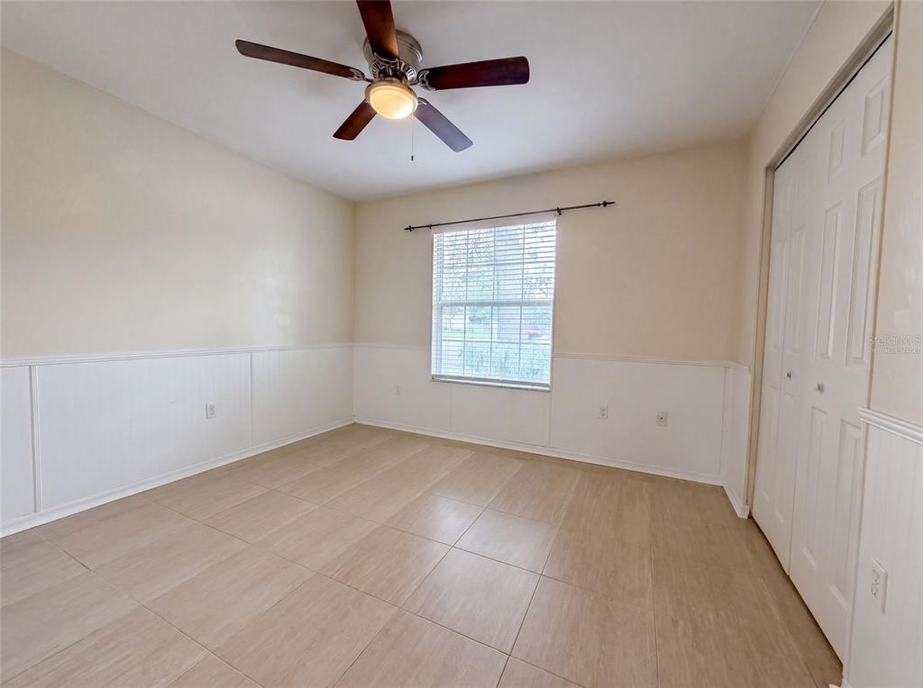 An empty bedroom features tile flooring, white wainscoting, a ceiling fan, and a window with blinds — 944 NW 87TH DRIVE, GAINESVILLE, FL
