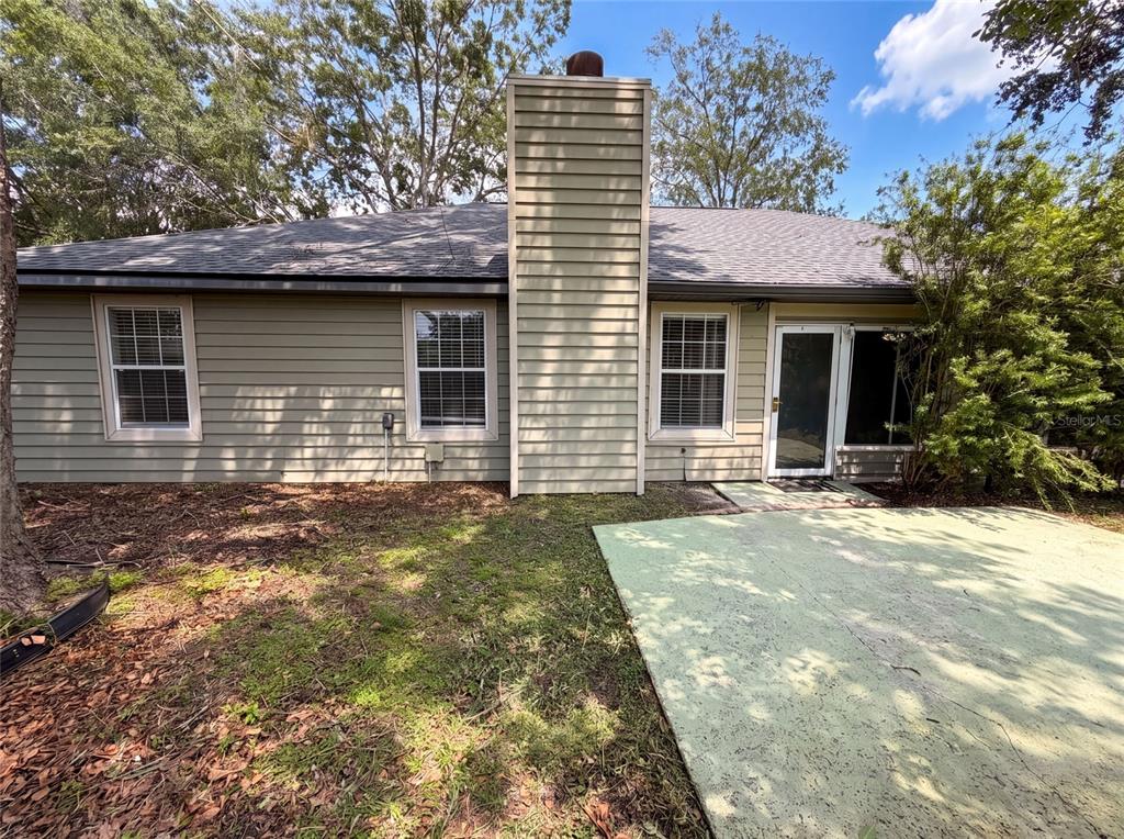 The exterior of a house features beige siding, a central chimney, and a concrete patio — 944 NW 87TH DRIVE, GAINESVILLE, FL