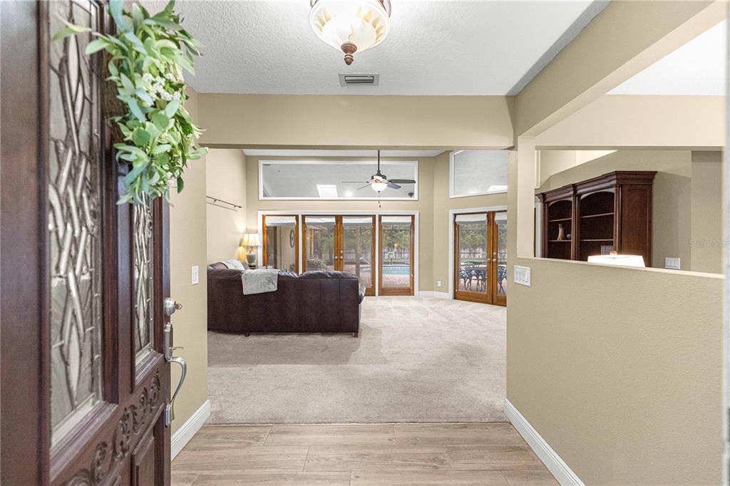 A view from an entryway into a living room with carpet, glass doors, and pool views — 1020 SW 32ND LANE, OCALA, FL