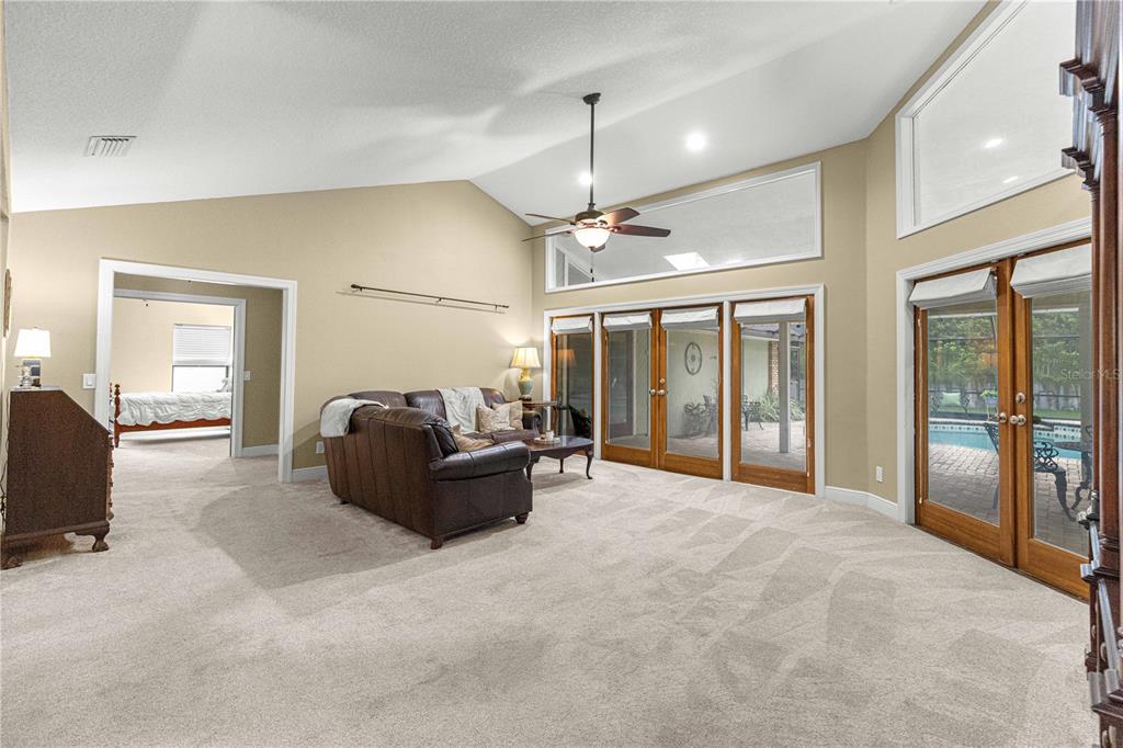 A living room with vaulted ceilings, beige carpet, a leather sofa, and glass patio doors — 1020 SW 32ND LANE, OCALA, FL