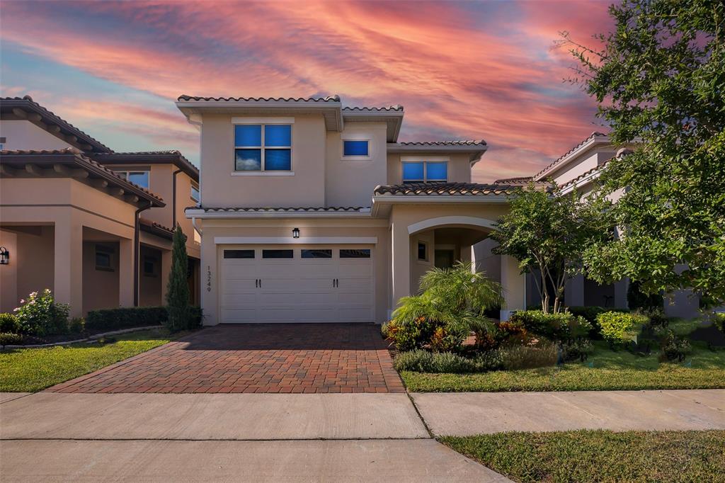 A two-story suburban house with a beige stucco exterior, a two-car garage, and a brick driveway — 13249 WINTERTON LANE, ORLANDO, FL