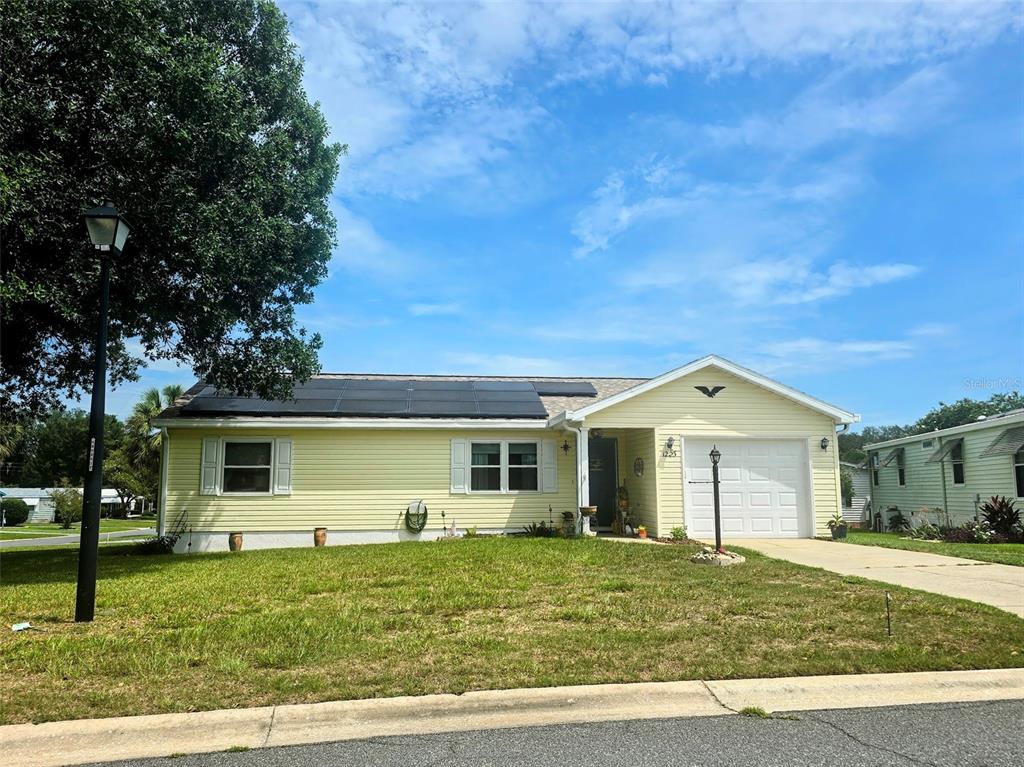 A single-story yellow house with solar panels on the roof and a front-facing garage — 1223 TARPON LANE, LADY LAKE, FL