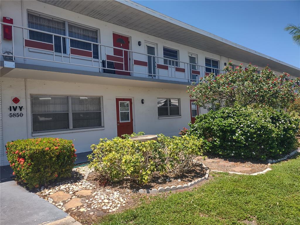 A two-story apartment building features white exterior walls, red doors, and a metal balcony railing — 5850 18TH STREET N UNIT 23, ST PETERSBURG, FL