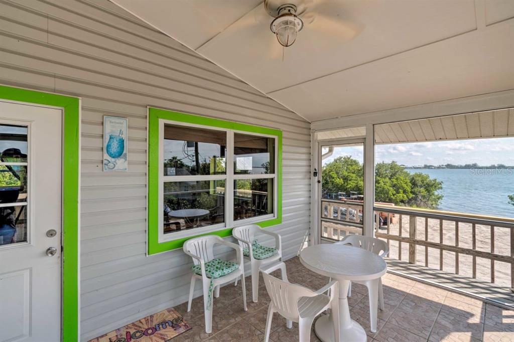A covered porch with white plastic chairs and a table overlooks a body of water — 8876 BAY STREET UNIT A, PLACIDA, FL