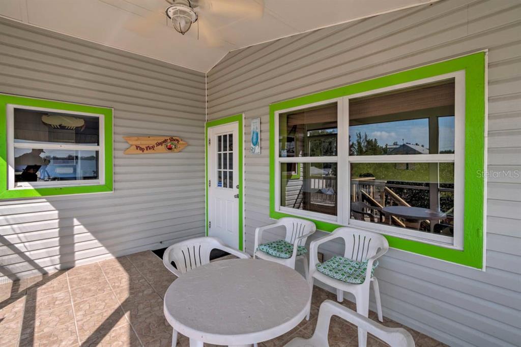 A covered porch features gray siding, bright green window trim, a table, and white chairs — 8876 BAY STREET UNIT A, PLACIDA, FL