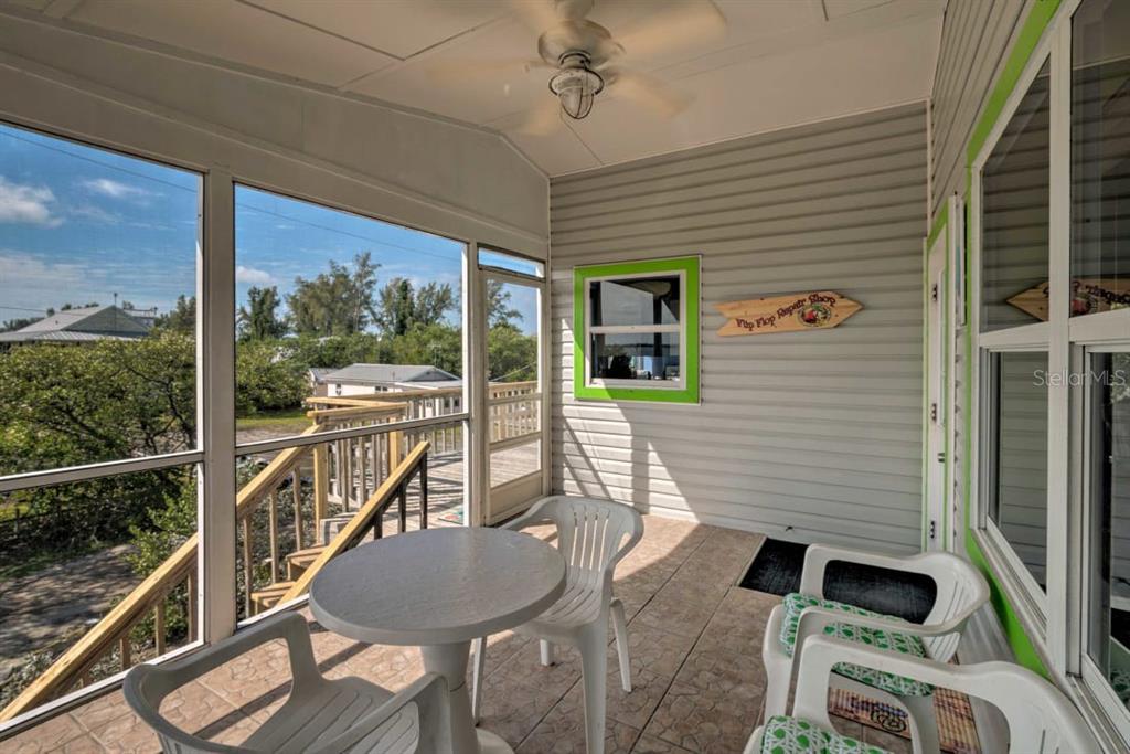 A screened-in porch features a round table, white plastic chairs, and a view of trees — 8876 BAY STREET UNIT A, PLACIDA, FL