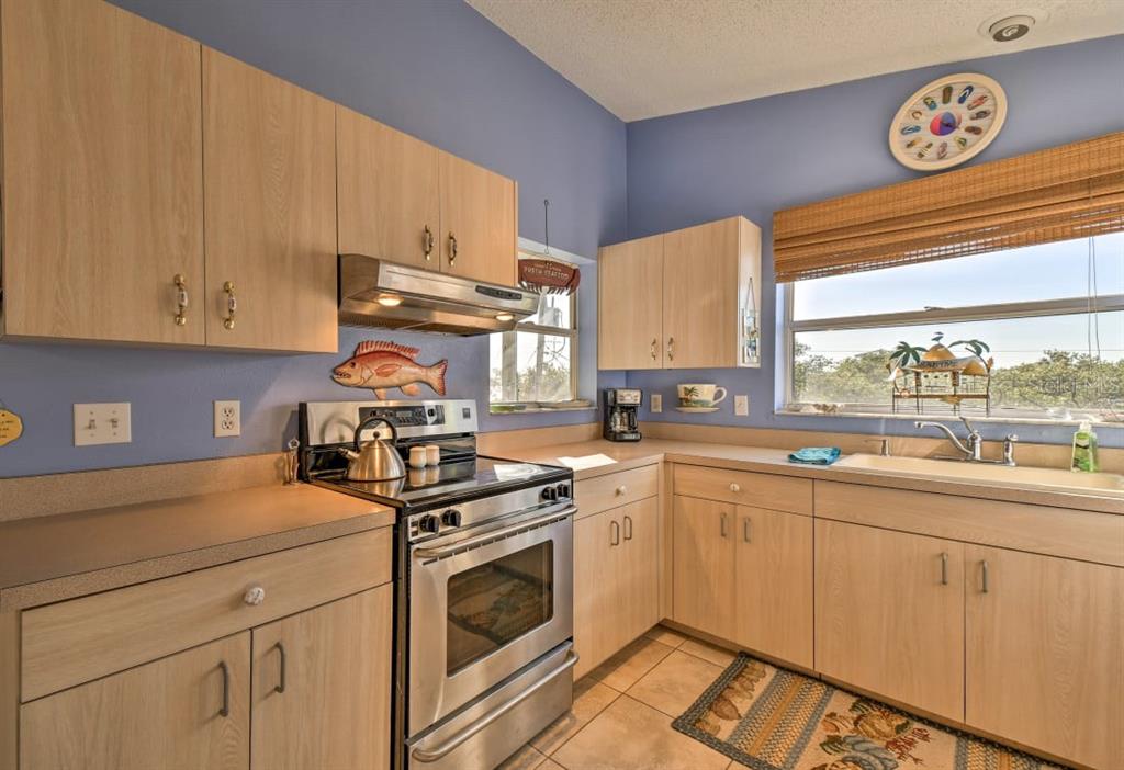 A kitchen with light wood cabinets, blue walls, a stainless steel stove, and a window — 8876 BAY STREET UNIT A, PLACIDA, FL