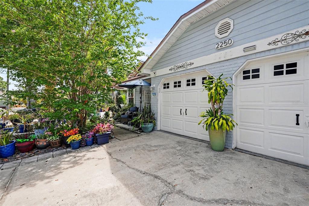 The exterior of a light blue house features a two-car garage and a potted garden — 2250 SPRINGWOOD CIR W, CLEARWATER, FL