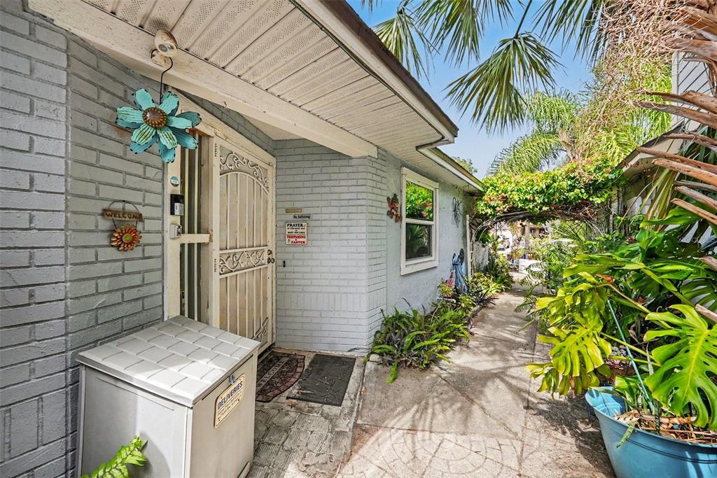A grey brick house exterior features a white security door, a delivery box, and landscaping — 2250 SPRINGWOOD CIR W, CLEARWATER, FL