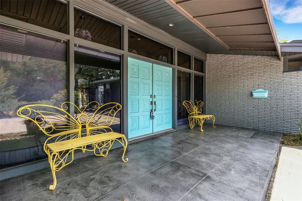 A covered porch features two yellow butterfly-shaped benches, a turquoise double door, and brick walls — 2634 COLLINS AVENUE, LAKELAND, FL