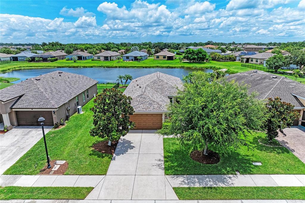 An aerial view shows three suburban houses with gray roofs and green lawns near a pond — 5706 106TH AVENUE E, PARRISH, FL