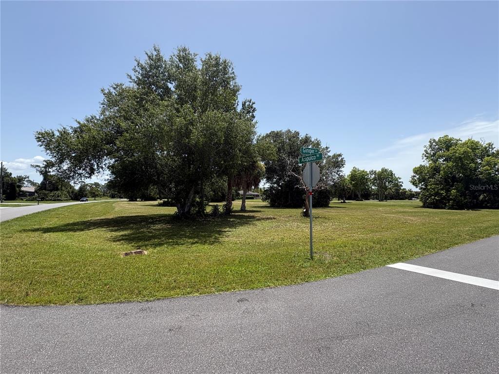 A grassy corner lot features a large tree and a street sign at an intersection — 16842 ACAPULCO ROAD, PUNTA GORDA, FL