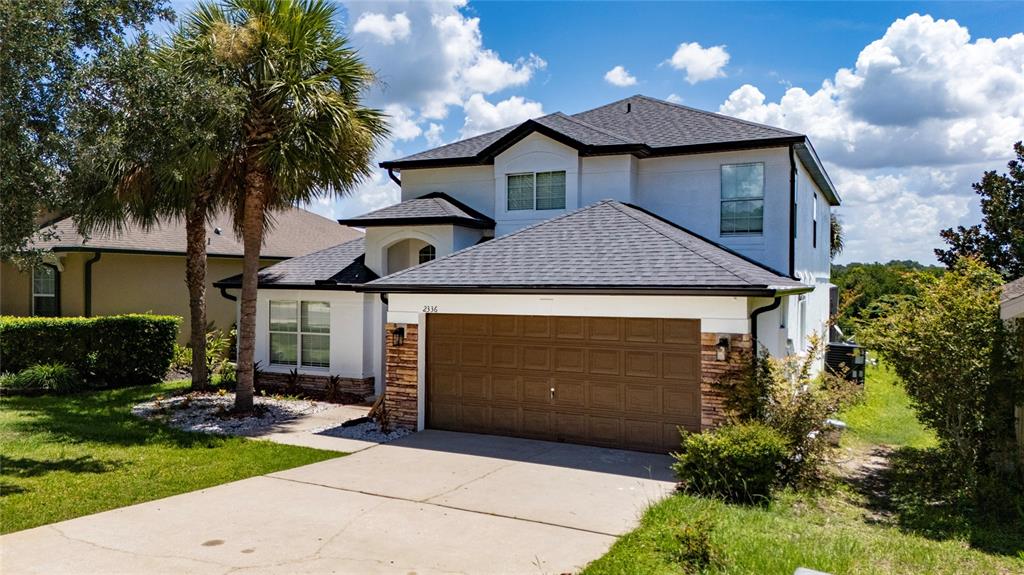A two-story house with a brown garage door, white stucco siding, and a palm tree — 2336 NATOMA BOULEVARD, MOUNT DORA, FL