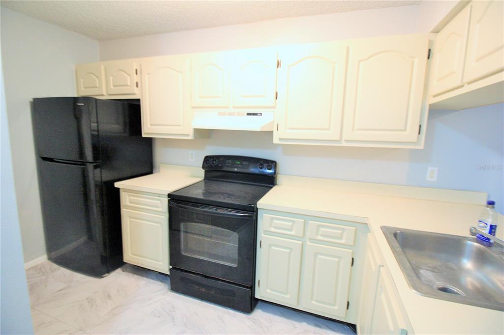 A kitchen features off-white cabinets, black appliances, light countertops, and a stainless steel sink — 660 KENWICK CIRCLE UNIT 104, CASSELBERRY, FL