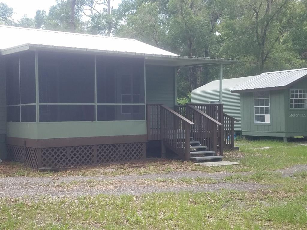 A green cabin with a screened porch and wooden stairs sits next to a shed — 40841 LOUISE ROAD, UMATILLA, FL
