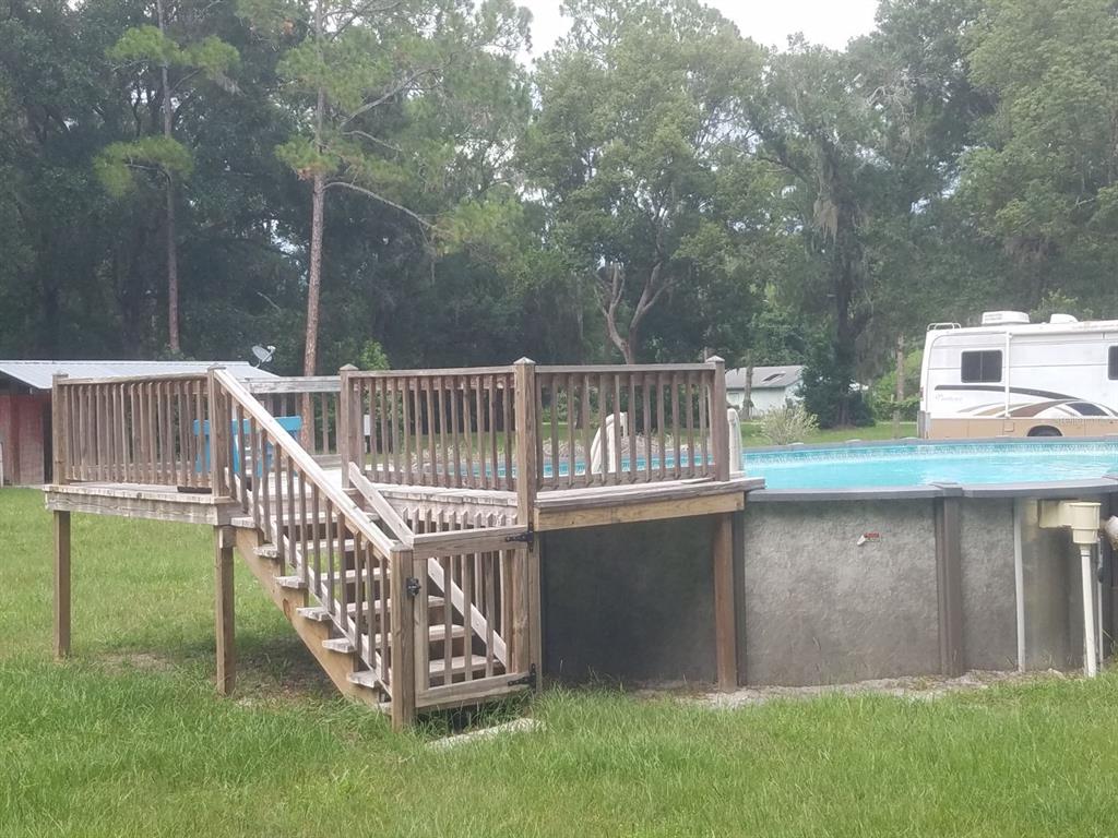 An above-ground swimming pool with an attached wooden deck and staircase in a grassy yard — 40841 LOUISE ROAD, UMATILLA, FL