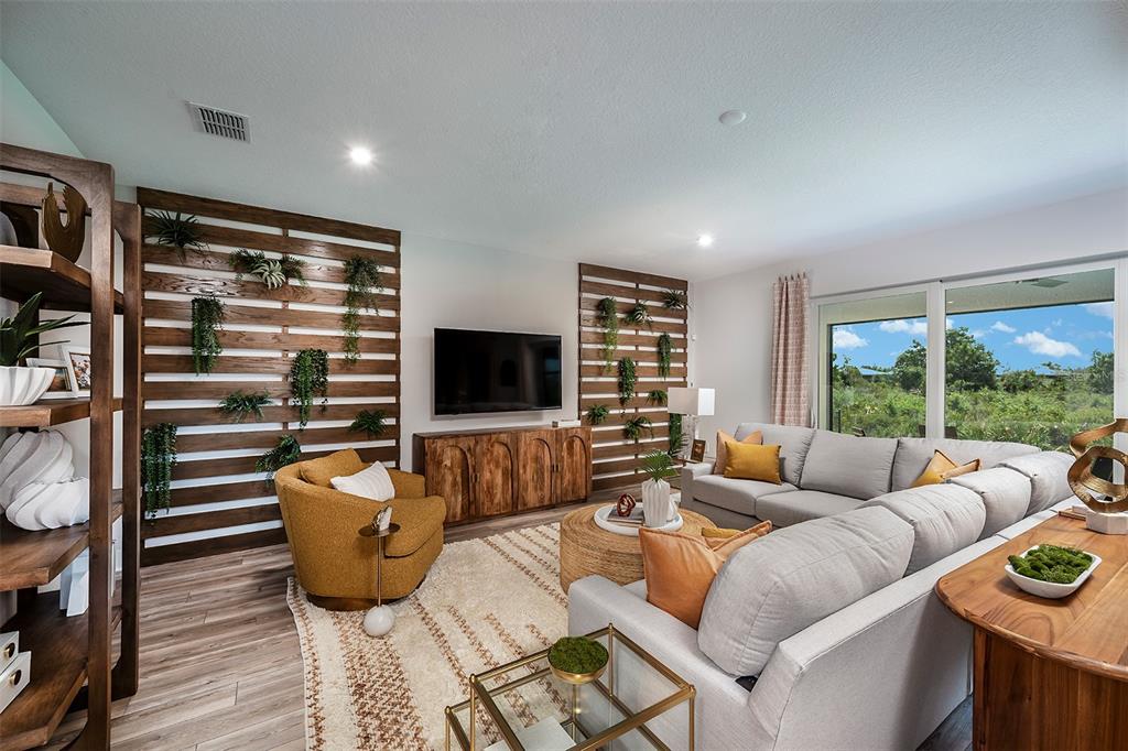 A living room features wood-slat accent walls with hanging plants, a sectional sofa, and furniture — 11965 STARBRIGHT PATH, VENICE, FL