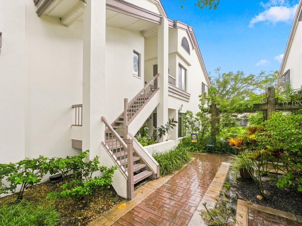 An exterior view of a white multi-story building with an outdoor staircase and brick walkway — 1816 LAKE CYPRESS DRIVE UNIT 1816, SAFETY HARBOR, FL