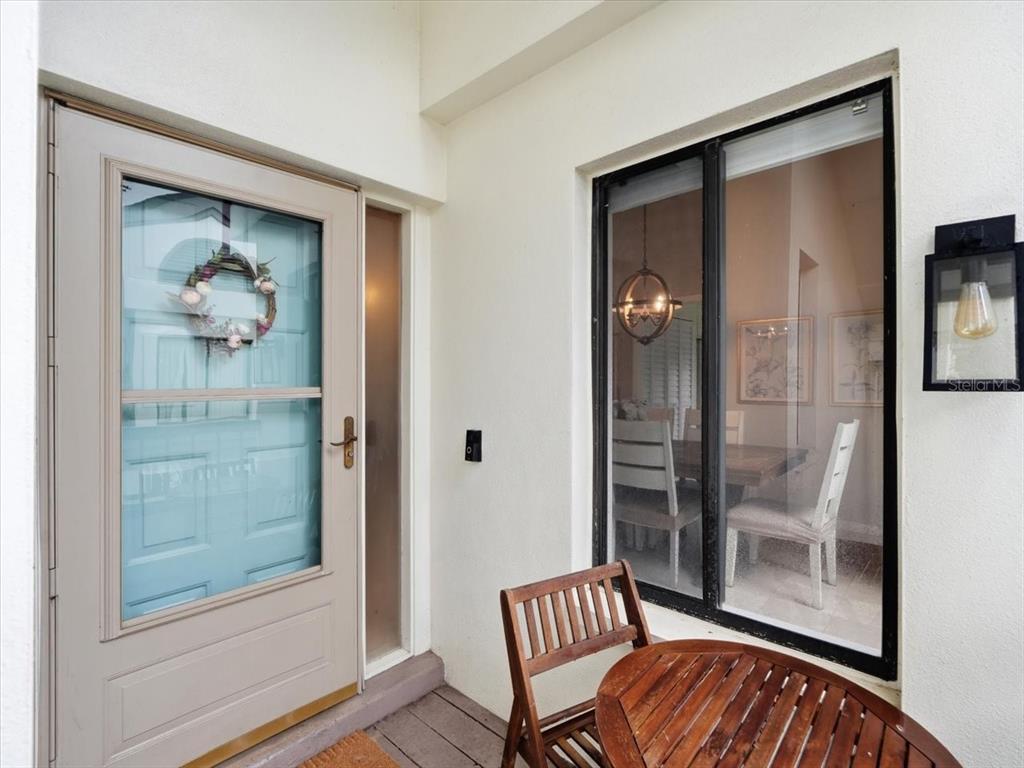 A light-colored front door with a wreath sits beside a window looking into a dining room — 1816 LAKE CYPRESS DRIVE UNIT 1816, SAFETY HARBOR, FL