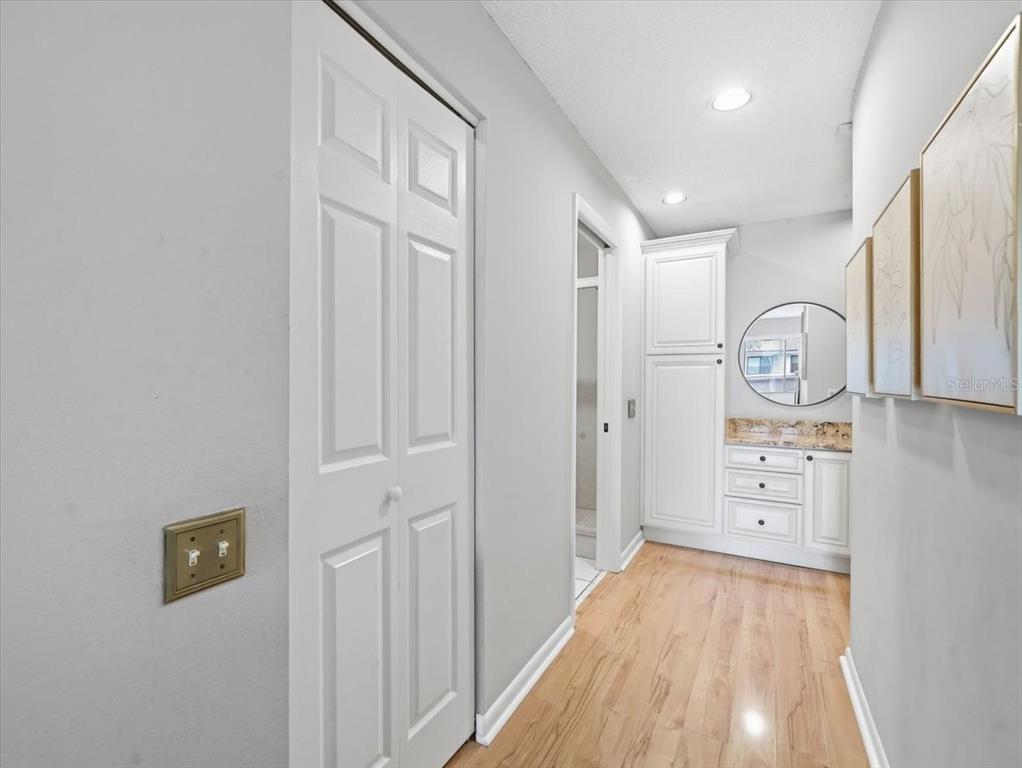 A hallway features light wood flooring, white cabinetry, a round mirror, and a bifold door — 1816 LAKE CYPRESS DRIVE UNIT 1816, SAFETY HARBOR, FL