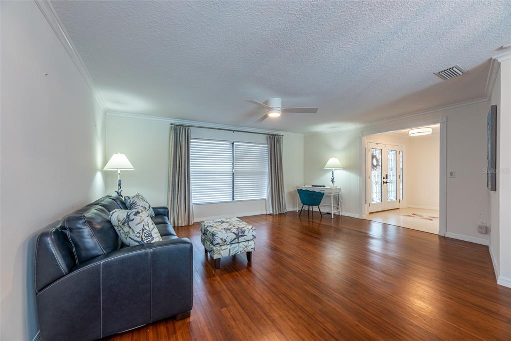 A living room features a dark leather sofa, patterned ottoman, hardwood floors, and a desk — 910 CHIPAWAY DRIVE, APOLLO BEACH, FL