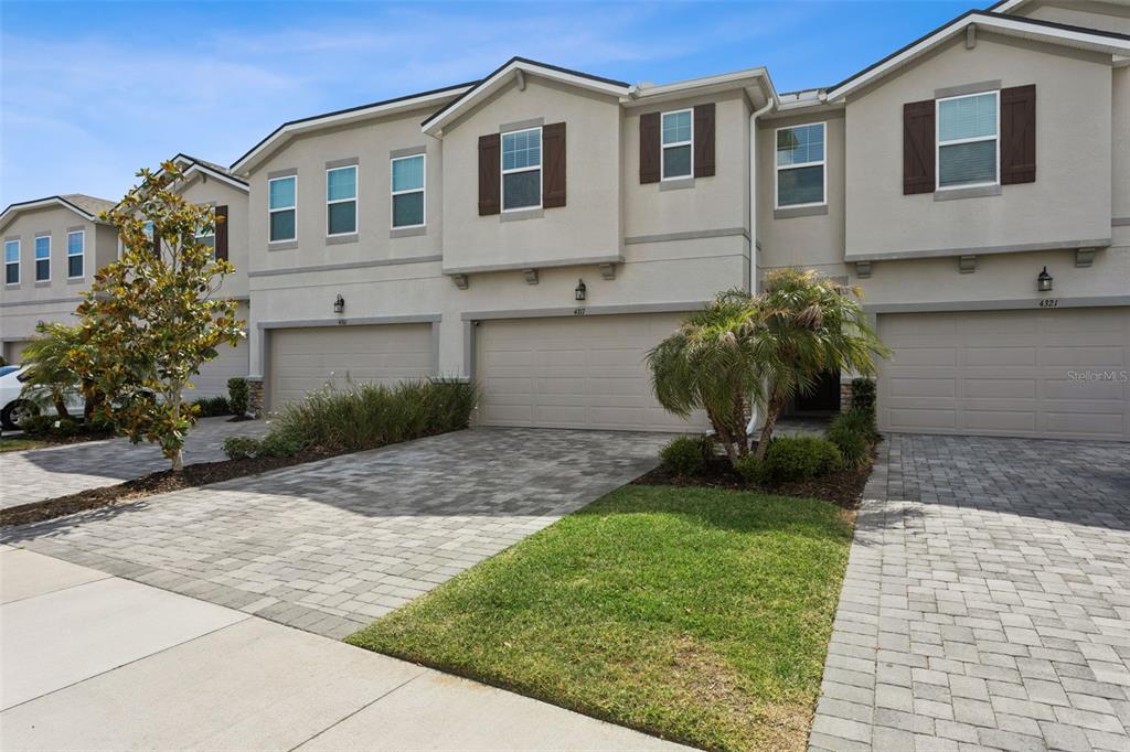 A row of three-story townhomes with beige stucco facades, brown shutters, and paved driveways — 4317 CLOUD HOPPER WAY, LUTZ, FL