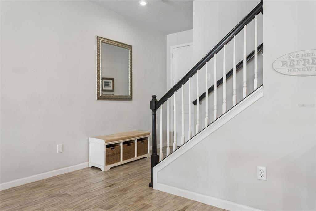 A foyer features a white storage bench, a wall mirror, and a staircase with railings — 4317 CLOUD HOPPER WAY, LUTZ, FL
