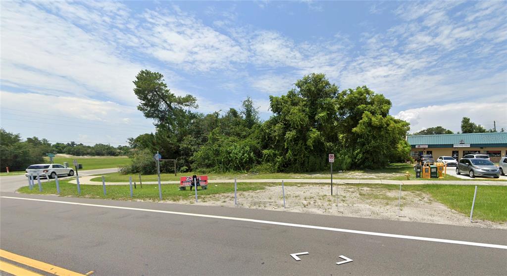 A vacant, grassy lot with trees and a sidewalk sits beside a commercial building — 1854 PROVIDENCE BOULEVARD, DELTONA, FL