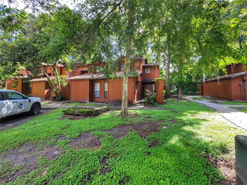 A two-story brown wood-sided townhouse sits behind a grassy yard with mature trees — 931 SW 57TH TERRACE, GAINESVILLE, FL