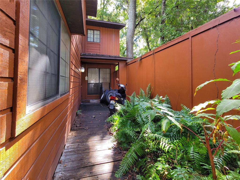 A wooden walkway leads to a house entrance beside a privacy fence and lush ferns — 931 SW 57TH TERRACE, GAINESVILLE, FL