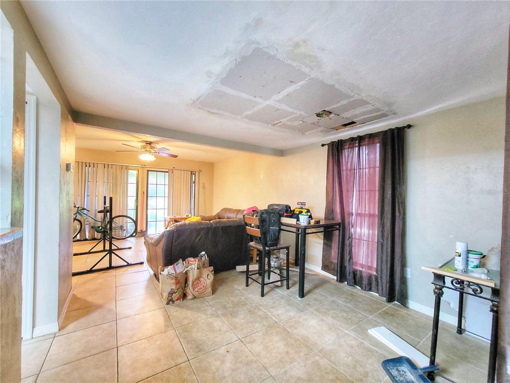 A living room with tile flooring, a brown leather sofa, and an unfinished ceiling patch — 931 SW 57TH TERRACE, GAINESVILLE, FL