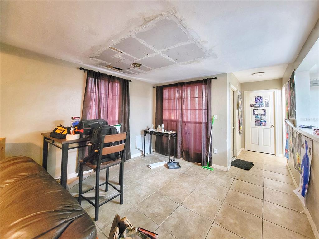 A room with tiled floors, dark curtains, a table, and a damaged section on the ceiling — 931 SW 57TH TERRACE, GAINESVILLE, FL