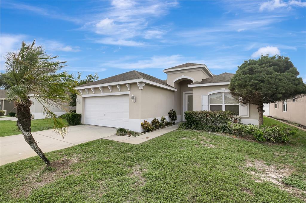 A single-story beige house with a two-car garage, a palm tree, and a front lawn — 14551 POTTERTON CIRCLE, HUDSON, FL