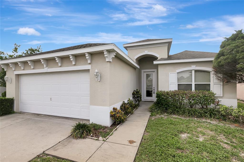 A single-story house with a white garage door, beige stucco exterior, and a front walkway — 14551 POTTERTON CIRCLE, HUDSON, FL