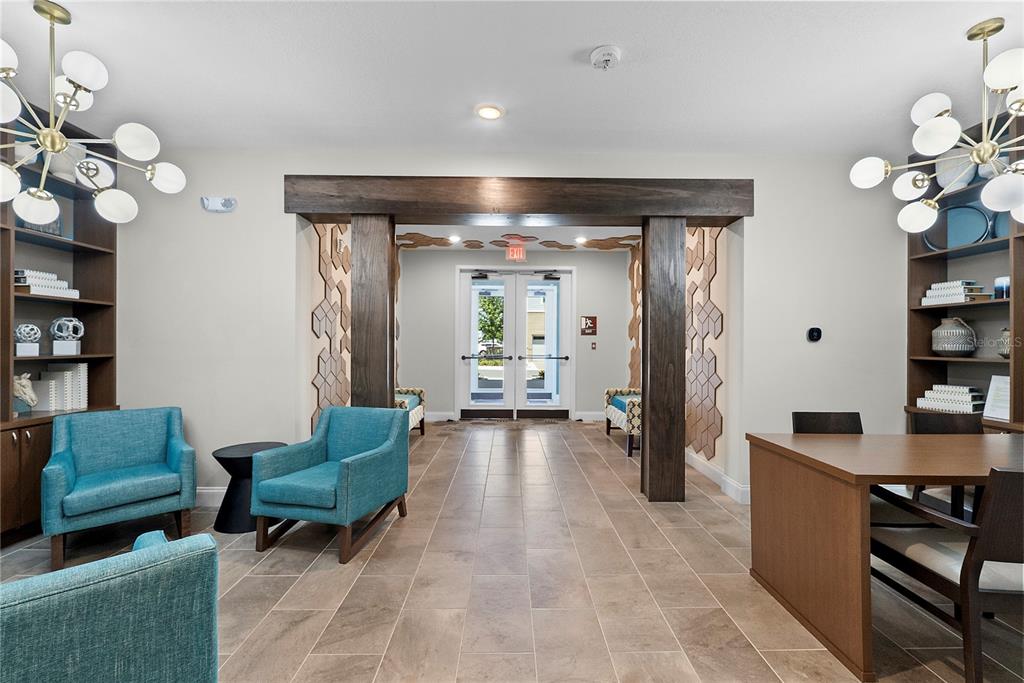 A lobby features teal armchairs, wood shelving, modern globe chandeliers, and a central doorway — 7557 LAUREATE BOULEVARD UNIT 6401, ORLANDO, FL