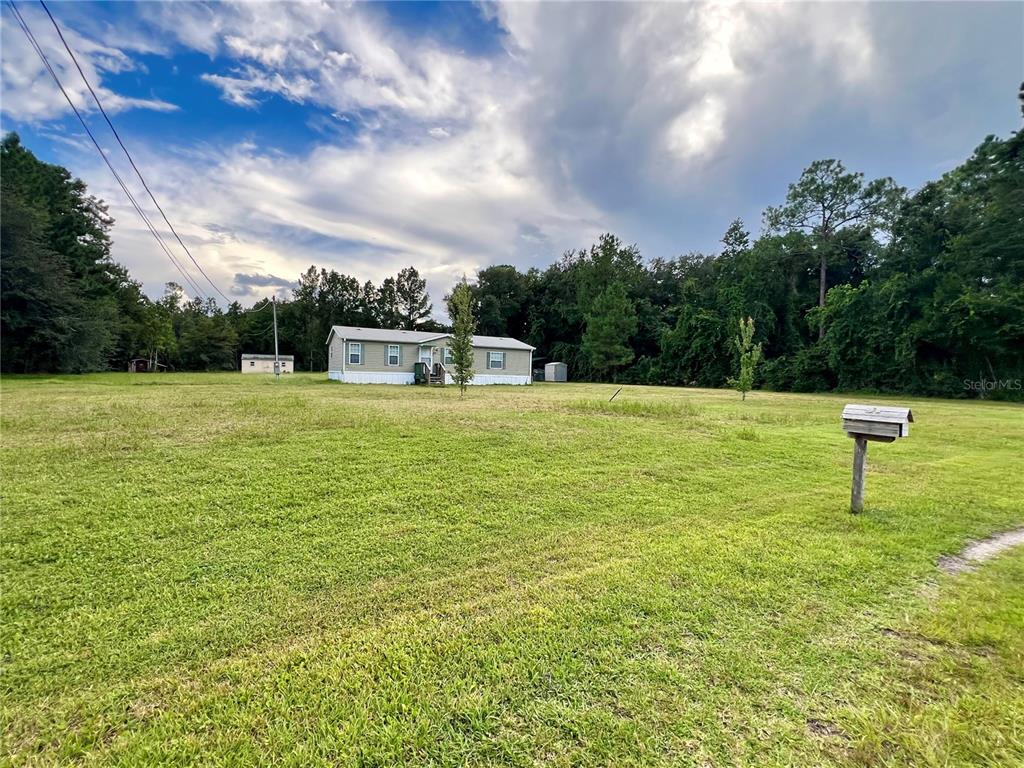 A single-story manufactured home sits on a large, grassy lot with scattered trees — 113 SABRINA LN, PALATKA, FL