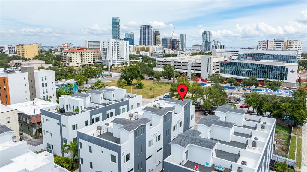 An aerial view shows modern white and gray townhouses with rooftop decks near a city skyline — 865 S 6 AVENUE S UNIT 17, ST PETERSBURG, FL