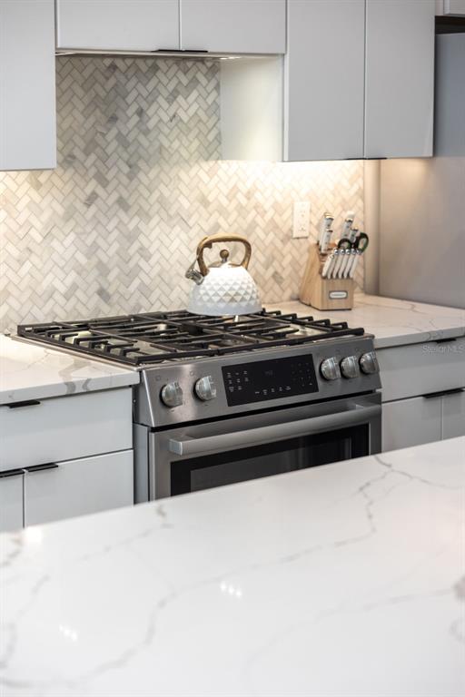A modern kitchen features white cabinets, a herringbone tile backsplash, and a stainless steel range — 865 S 6 AVENUE S UNIT 17, ST PETERSBURG, FL
