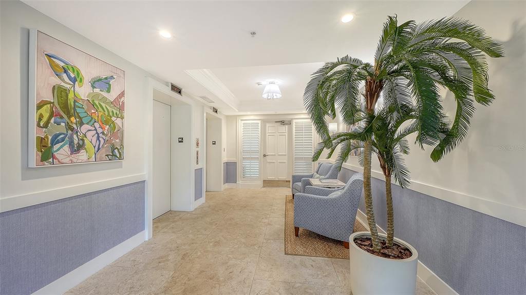 A bright building lobby features tile floors, two blue armchairs, a potted palm, and artwork — 409 NORTH POINT ROAD UNIT 401, OSPREY, FL
