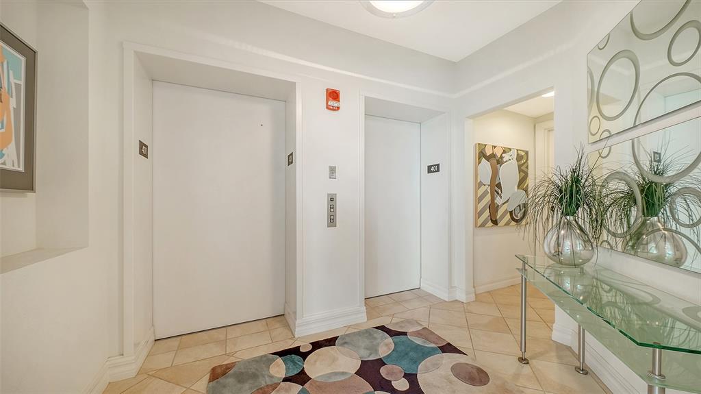 An elevator lobby features white doors, tiled floors, a patterned rug, and a glass console table — 409 NORTH POINT ROAD UNIT 401, OSPREY, FL