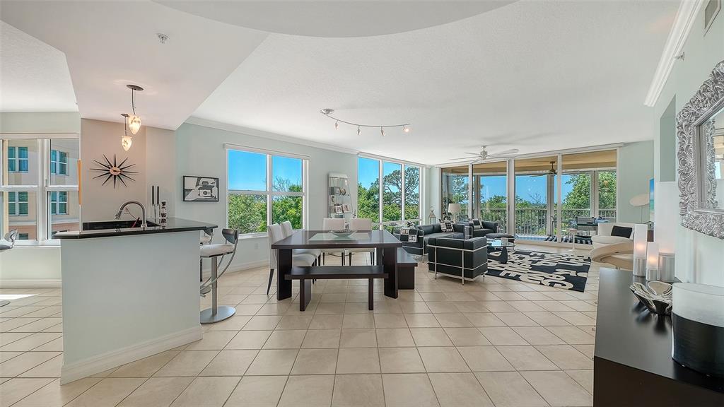 An open-concept living and dining area features tile flooring, large windows, and modern furniture — 409 NORTH POINT ROAD UNIT 401, OSPREY, FL